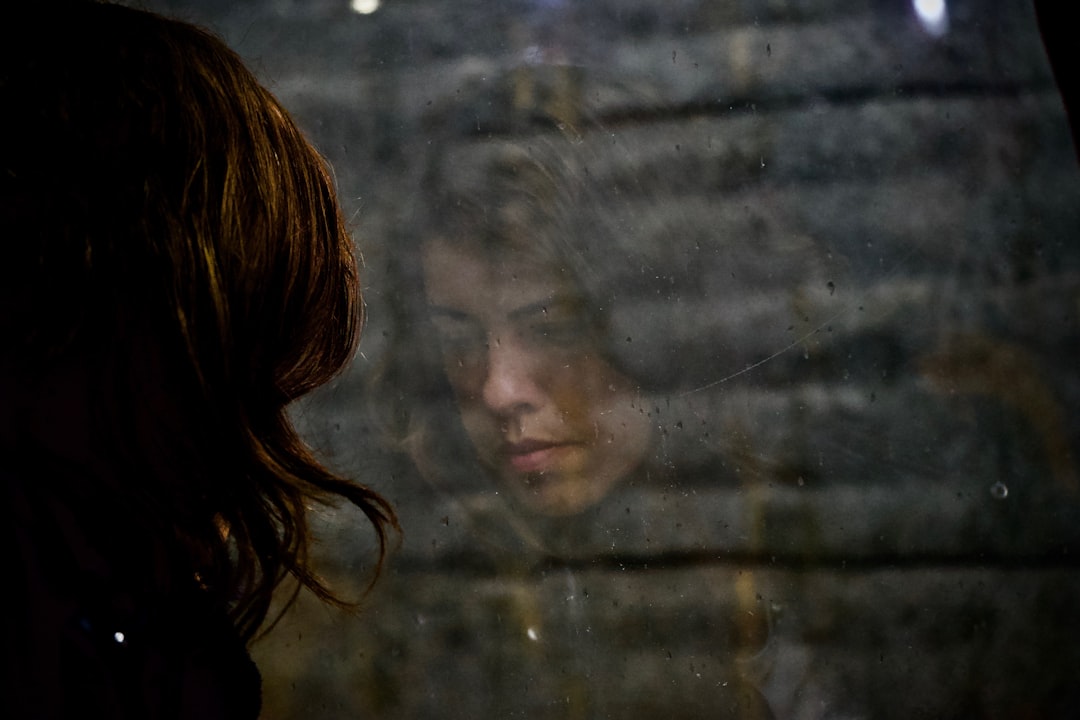 woman sitting on black chair in front of glass-panel window with white curtains